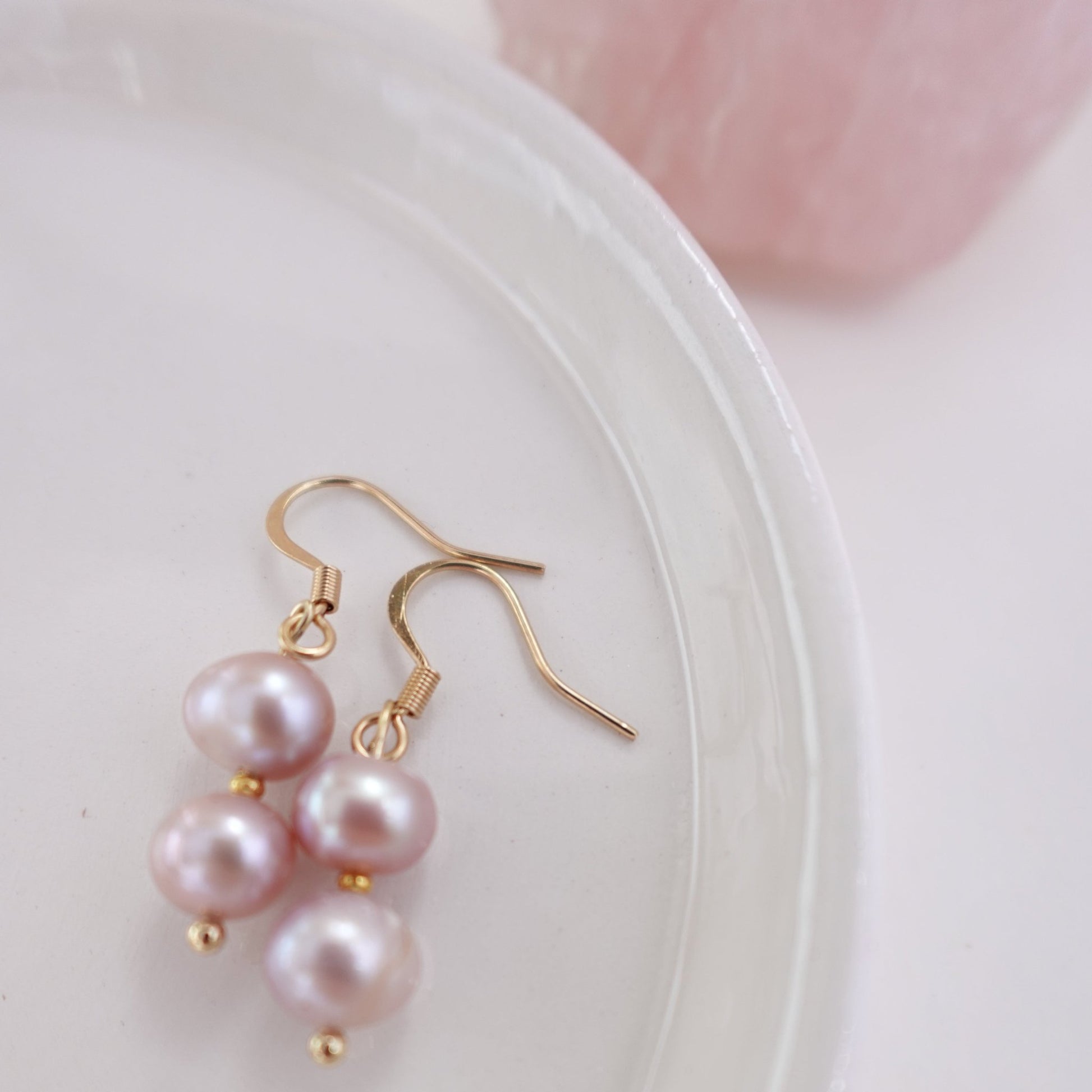 pink pearls with gold plated 18c dangle hardware laying on a ceramic plate with rose quart healing crystal