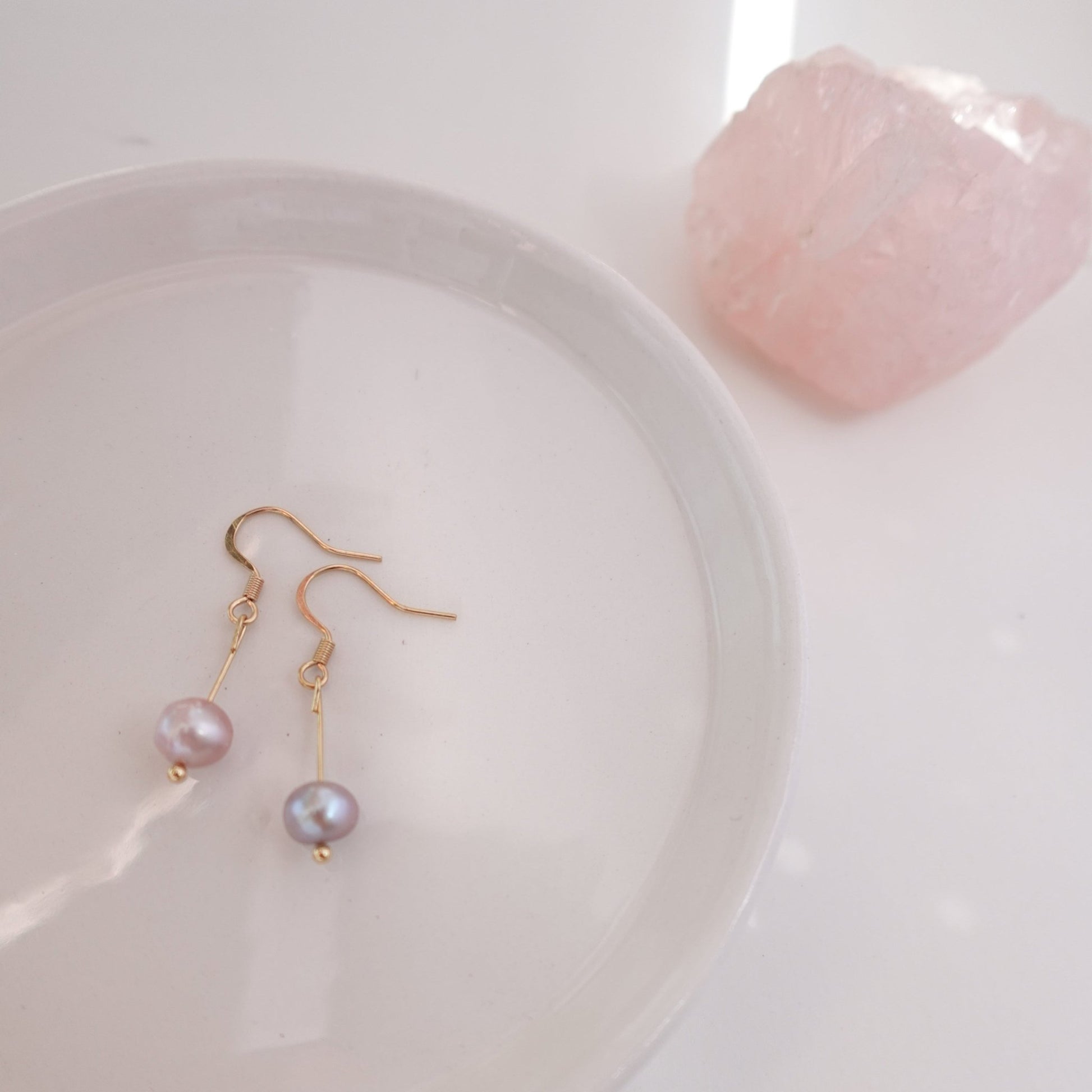 pink pearls with gold plated 18c dangle hardware laying on a ceramic plate with rose quart healing crystal