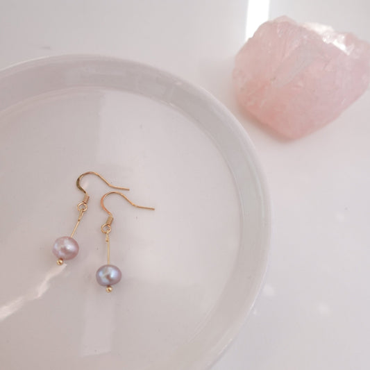 pink pearls with gold plated 18c dangle hardware laying on a ceramic plate with rose quart healing crystal