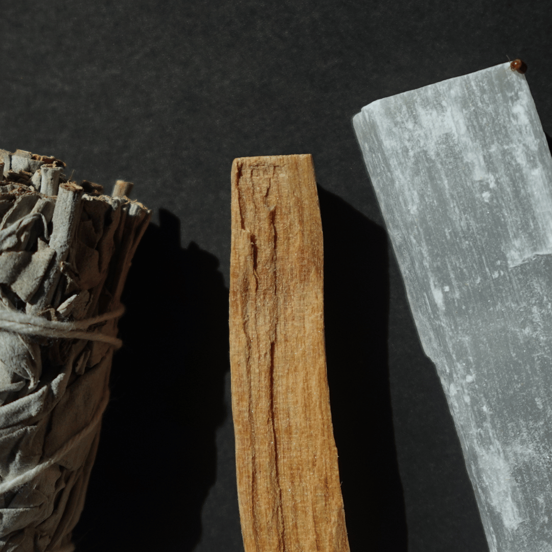 sage, palo santos and selenite crystal laying on a simple background
