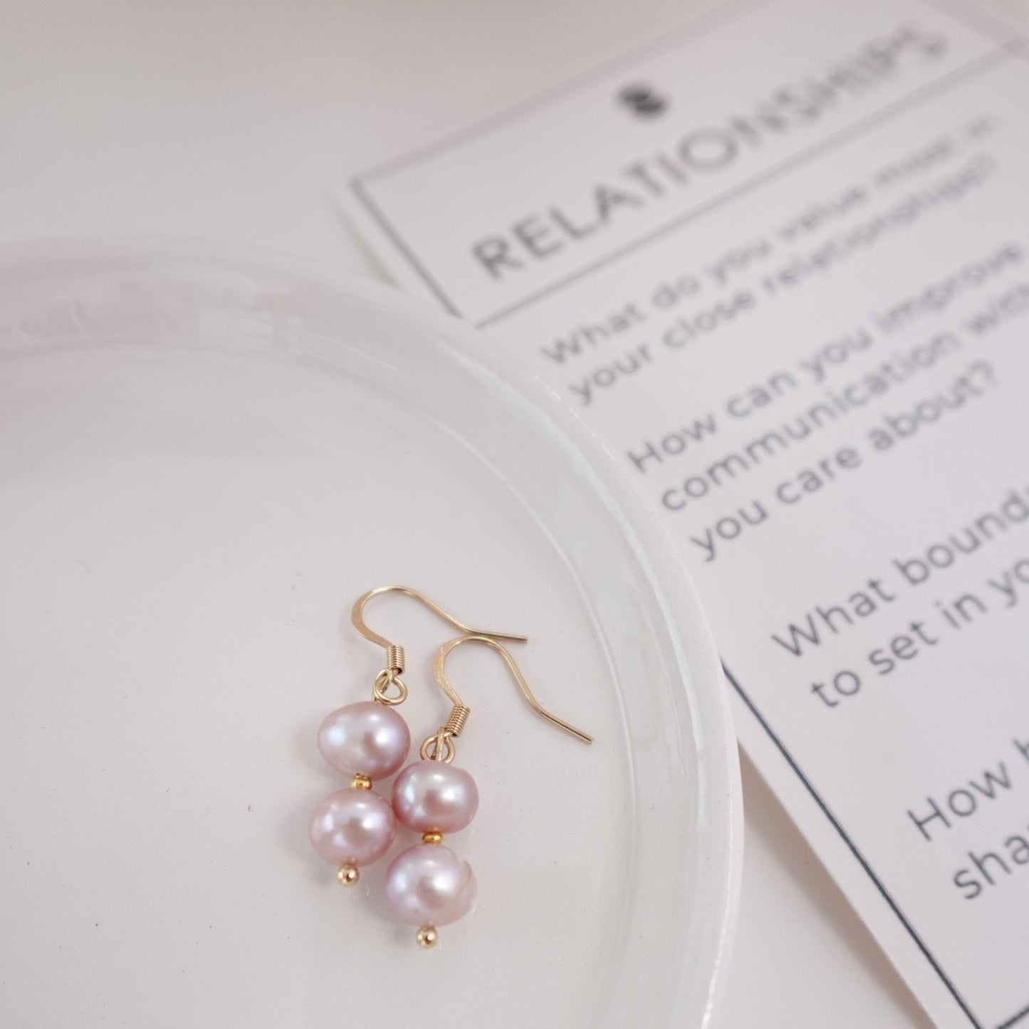pink pearls with gold plated 18c dangle hardware laying on a ceramic plate with rose quart healing crystal