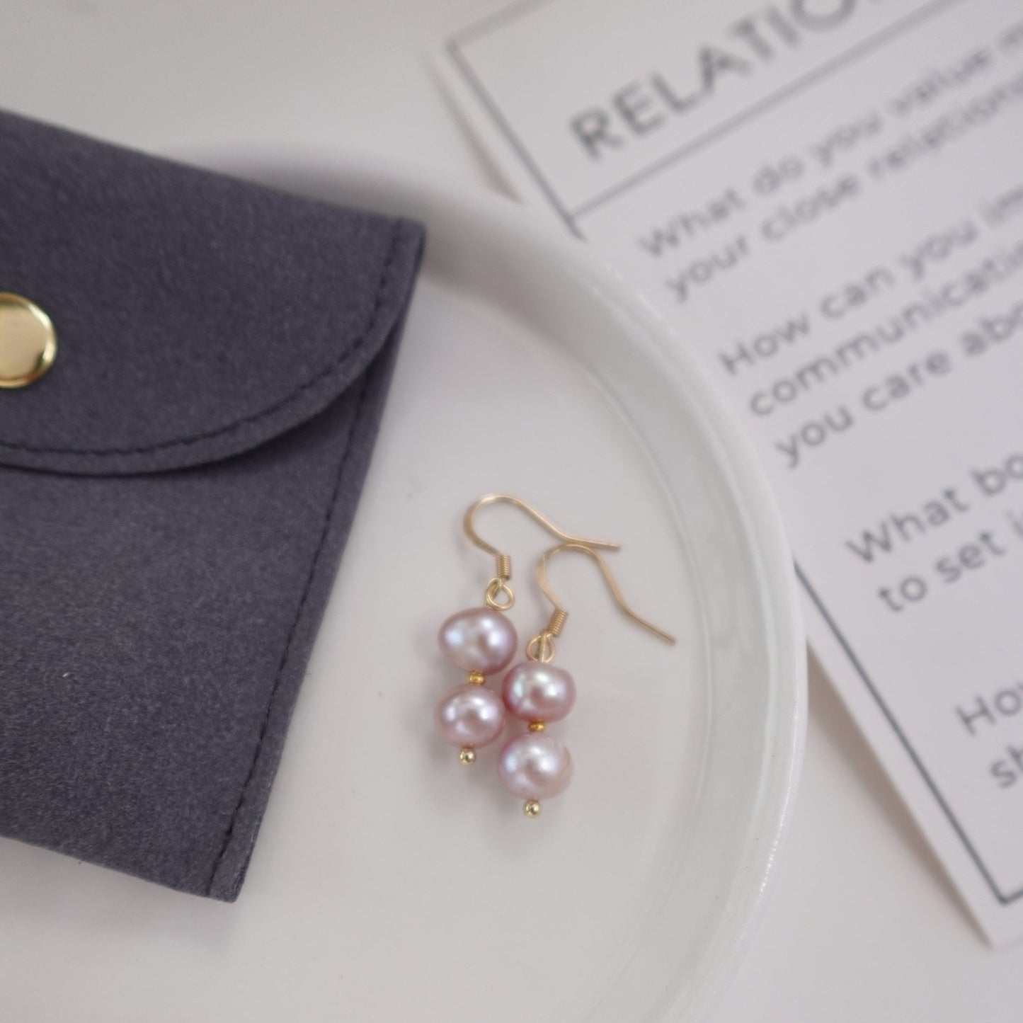 pink pearls with gold plated 18c dangle hardware laying on a ceramic plate with grey gift pouch and meaningful ritual card for gift set