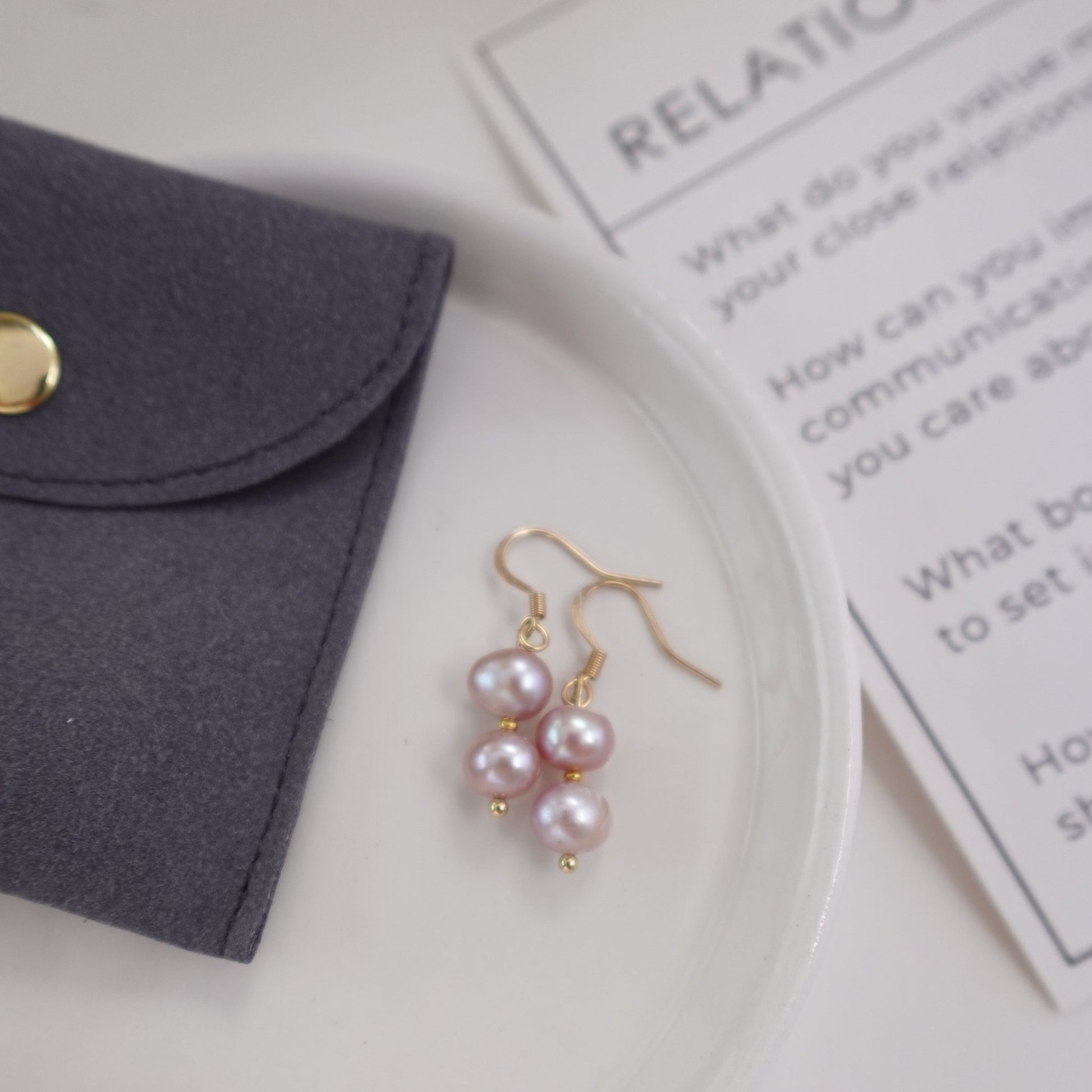 pink pearls with gold plated 18c dangle hardware laying on a ceramic plate with grey gift pouch and meaningful ritual card for gift set