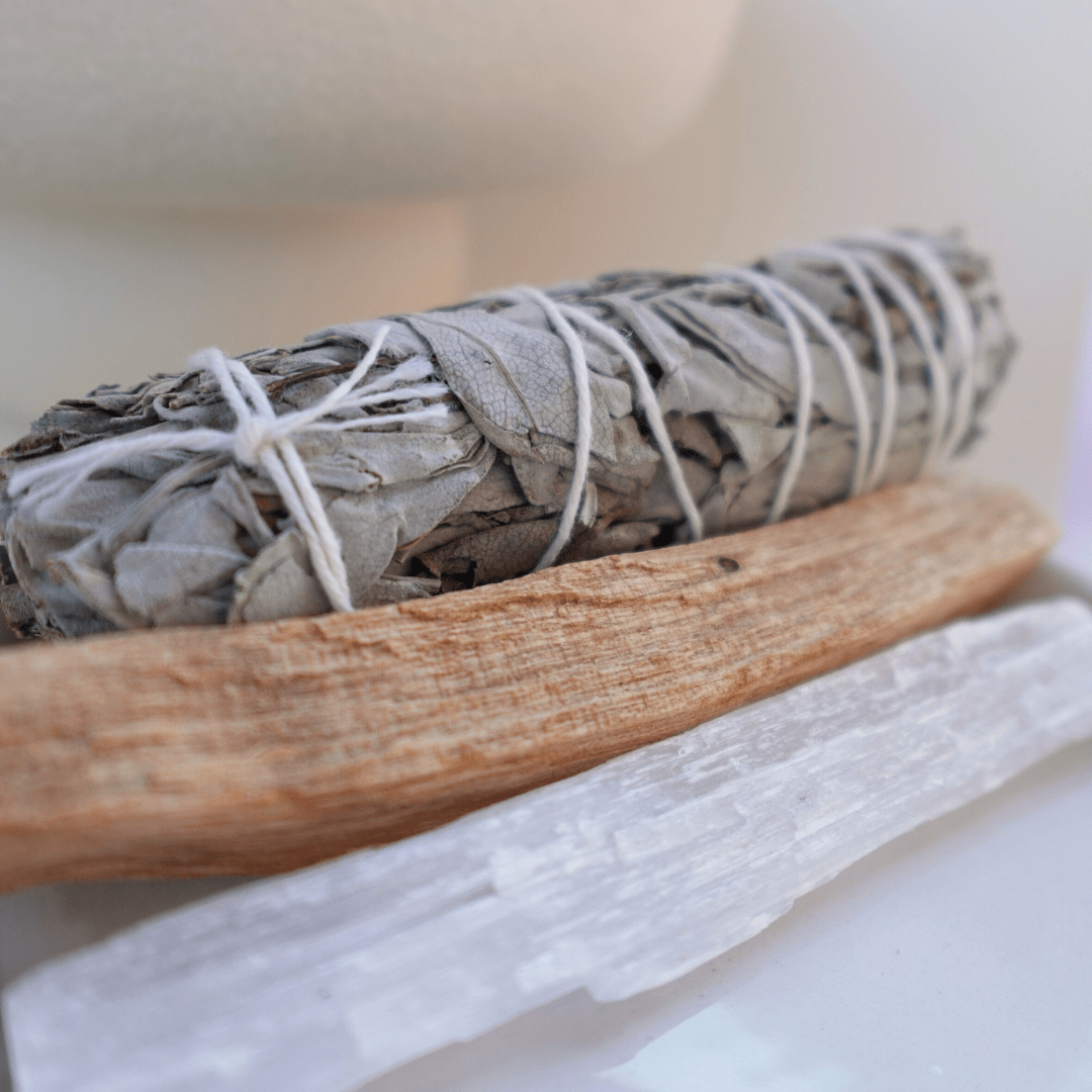 Sage bundle tied with white string on a wooden stick against a neutral background
