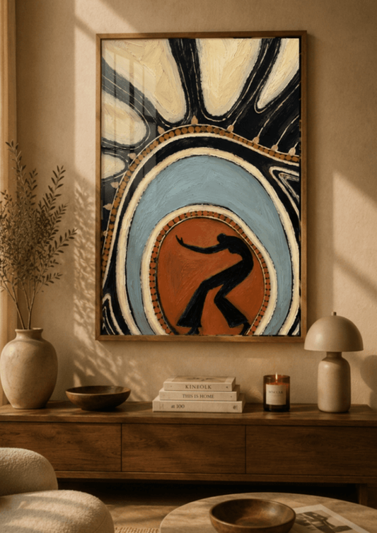 A framed abstract art print featuring a stylized dancer silhouette in a warm orange-brown center, surrounded by concentric blue, cream, and black shapes, hanging on a beige wall above a wooden console table in a styled room.
