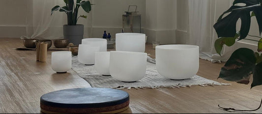 Yoga studio with white singing bowls, plants, and wooden floor.