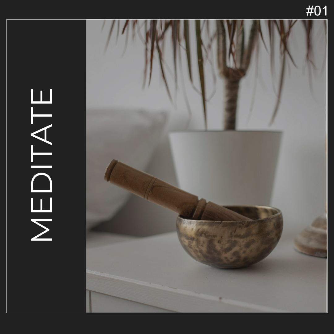 metal singing bowl with striker on white surface infront of a plant in white vase with text that reads meditate