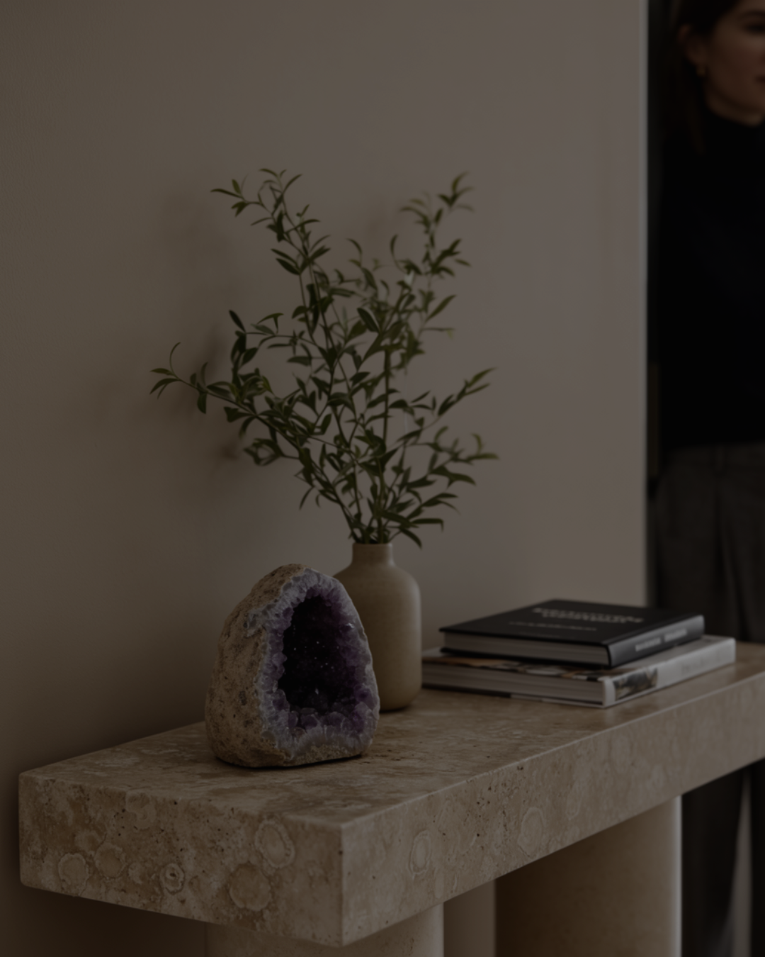 Decorative amethyst cave stone with purple accents on a stone surface next to a vase with greenery and books. home living decor.