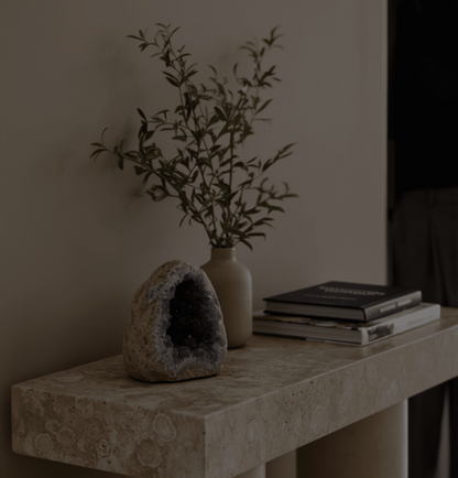 Decorative amethyst cave stone with purple accents on a stone surface next to a vase with greenery and books. home living decor.