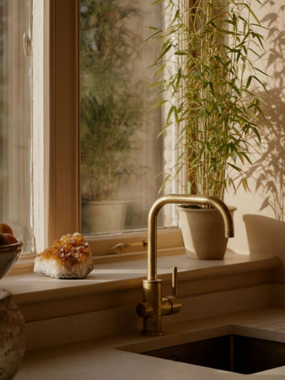 Kitchen sink with gold faucet and plants in the background citrine crystal resting on the windowsill