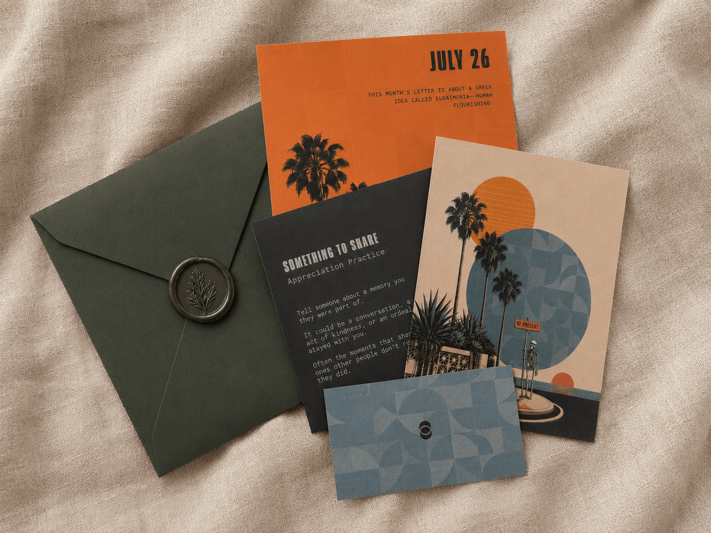 A sage green envelope with a green wax seal, with 4 artistic inserts laid next to it on a linen sheet. an art postcard, journal prompt card, note card and a letter about the concept of eudaemonia