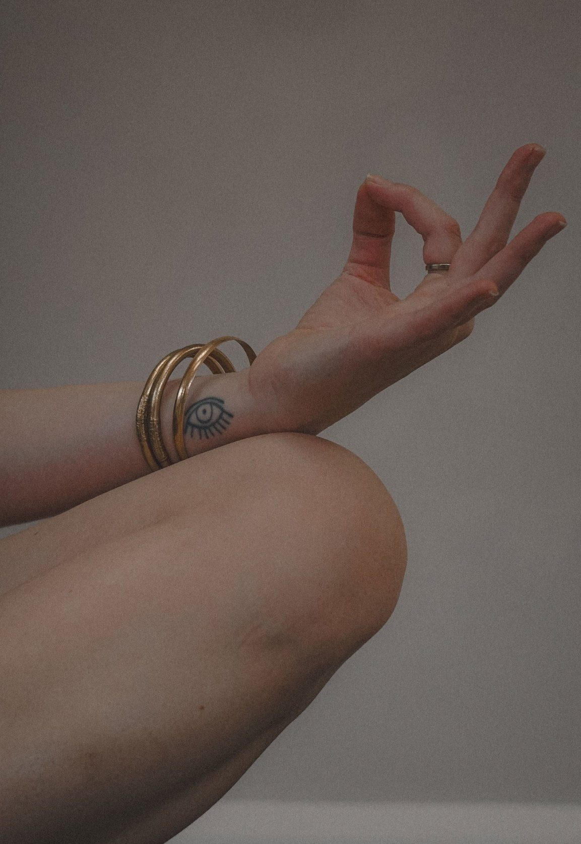 Hand with gold rings and a tattoo on a neutral background in a meditative pose