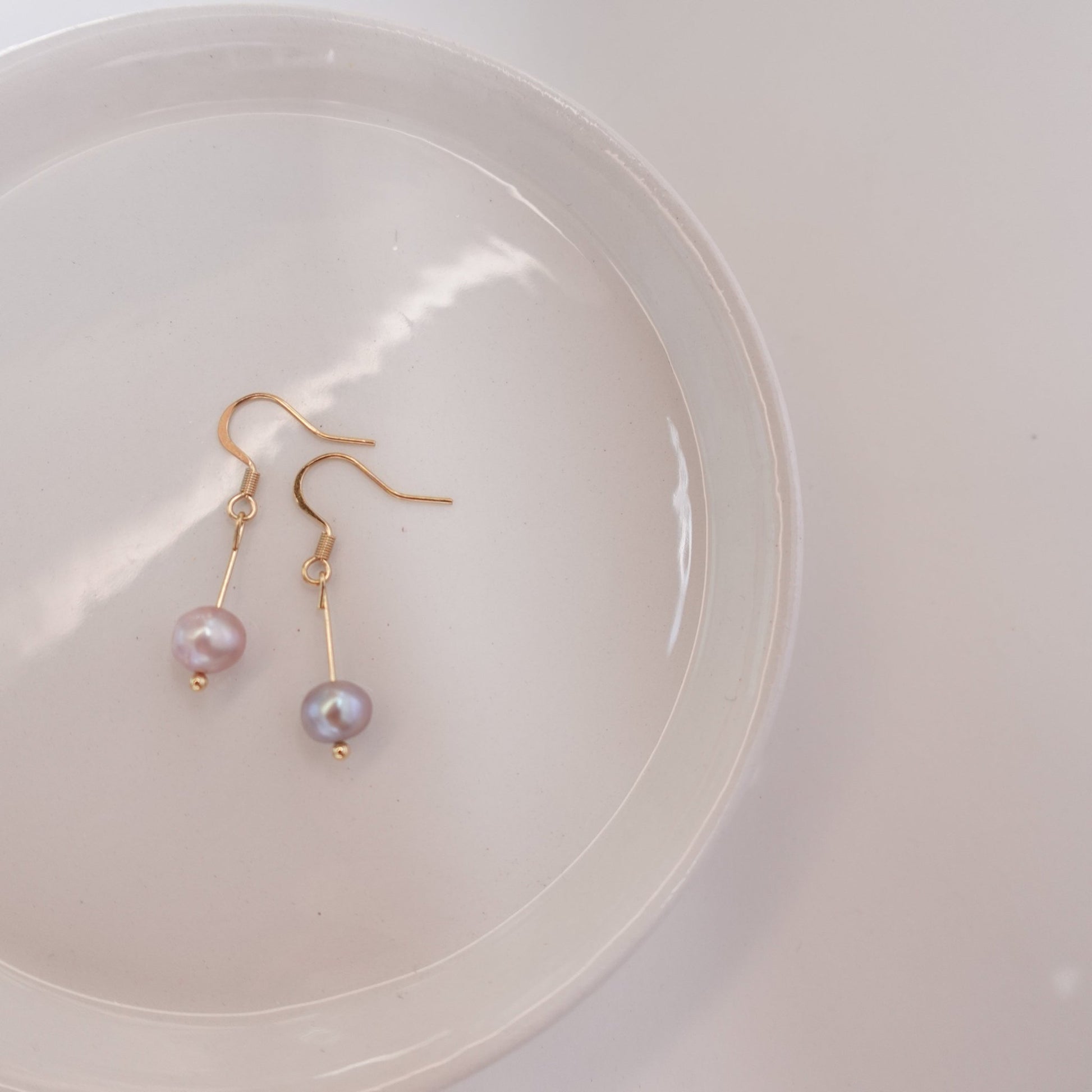 pink pearls with gold plated 18c dangle hardware laying on a ceramic plate 