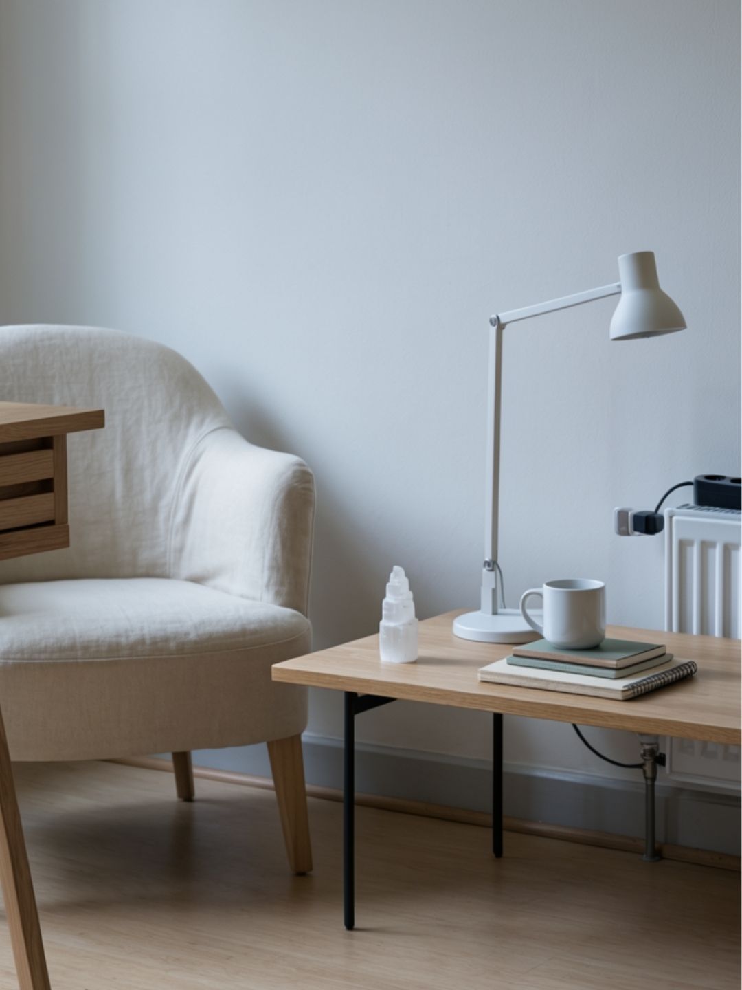 Minimalist living room with a beige armchair, wooden coffee table, selenite tower and lamp.