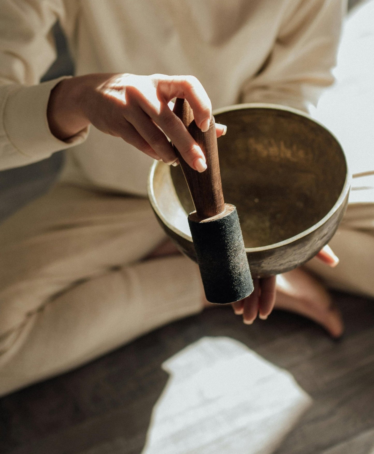 Person holding a singing bowl with a mallet in a blurred indoor setting