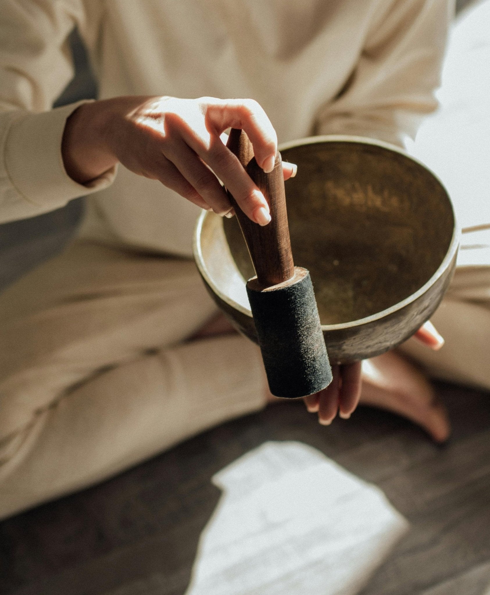 Person holding a singing bowl with a mallet in a blurred indoor setting