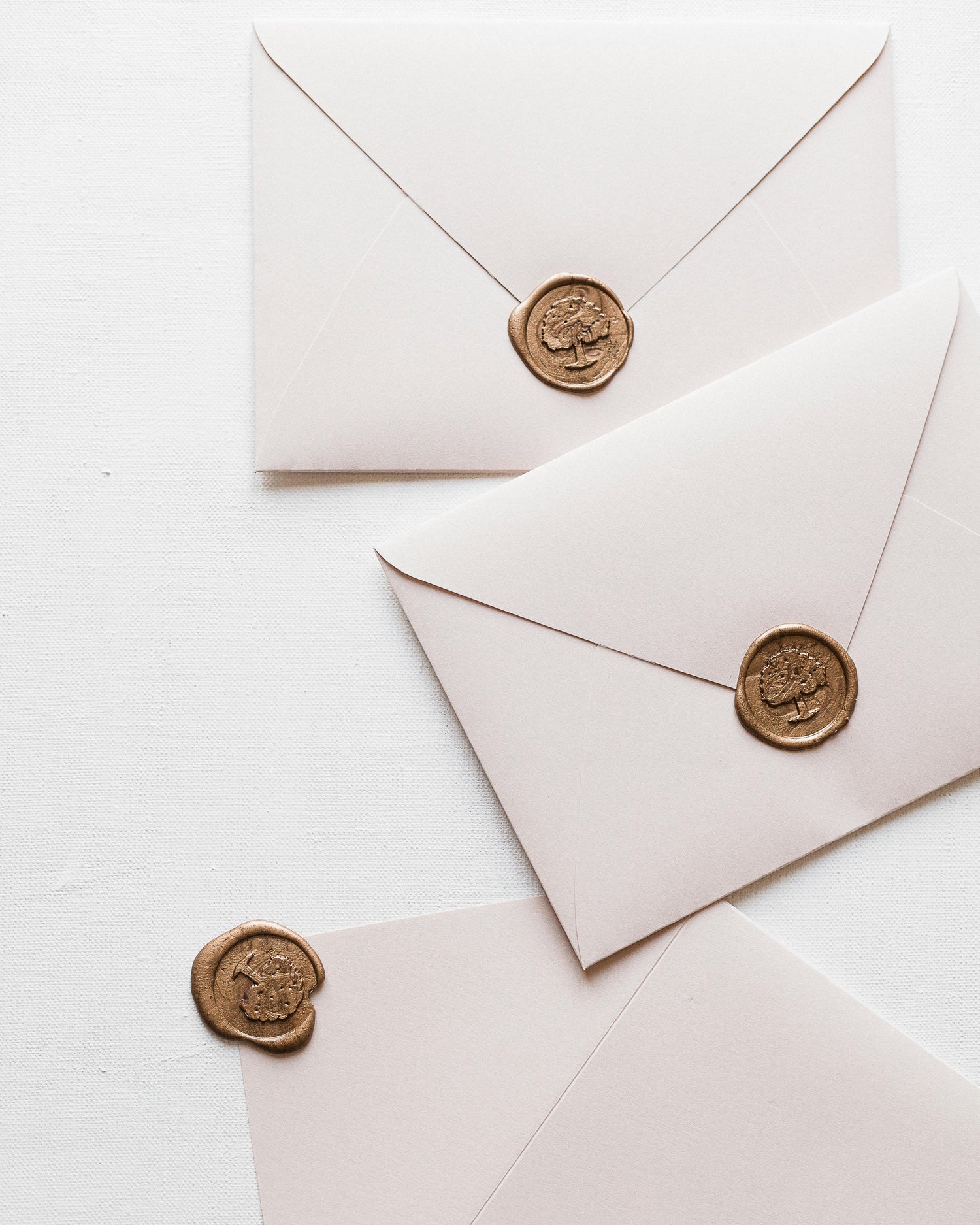 Three white envelopes with gold wax seals on a light background