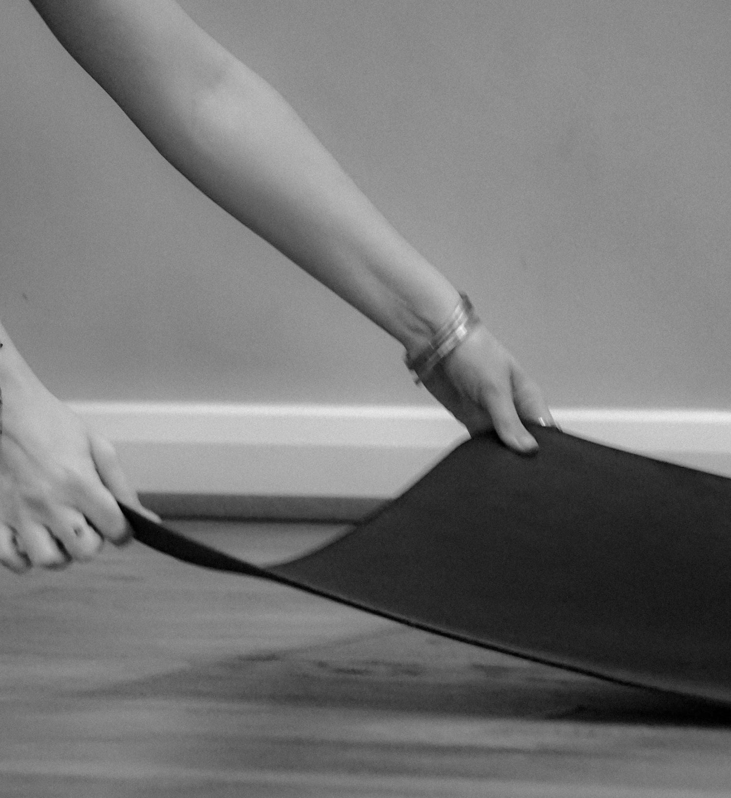 Person rolling out a yoga mat on a wooden floor.
